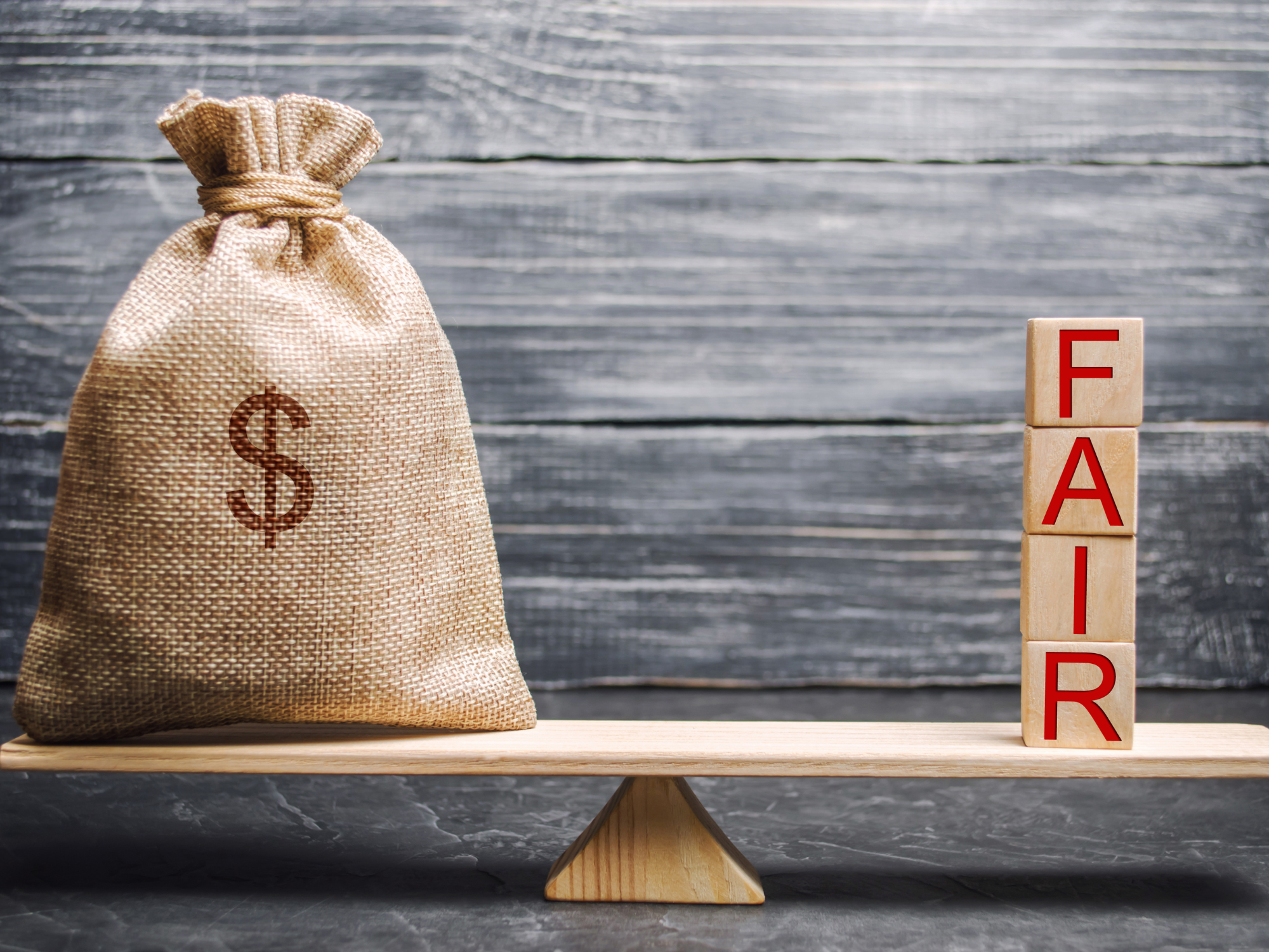 A scale weighing a bag of money and block letters that spell the word fair.