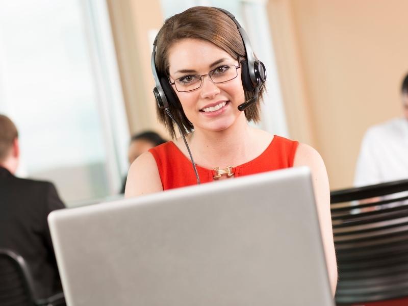 Woman working in a tech job with a headset and laptop computer wearing glasses